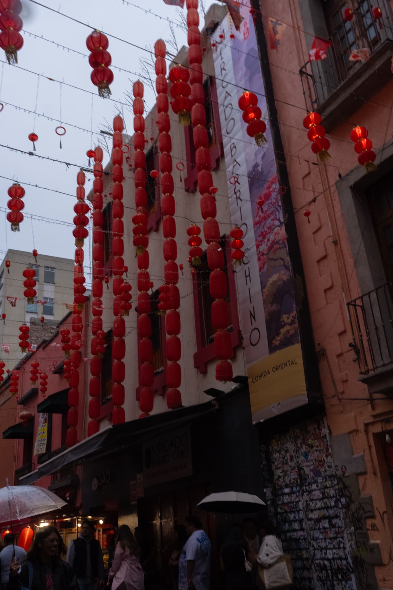 Rows of red paper lanterns strung between buildings over a narrow street at dusk